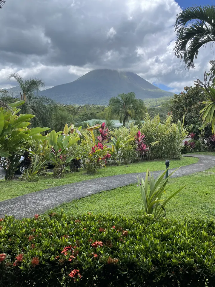 Arenal Volcano's cone rising behind a flower-filled garden